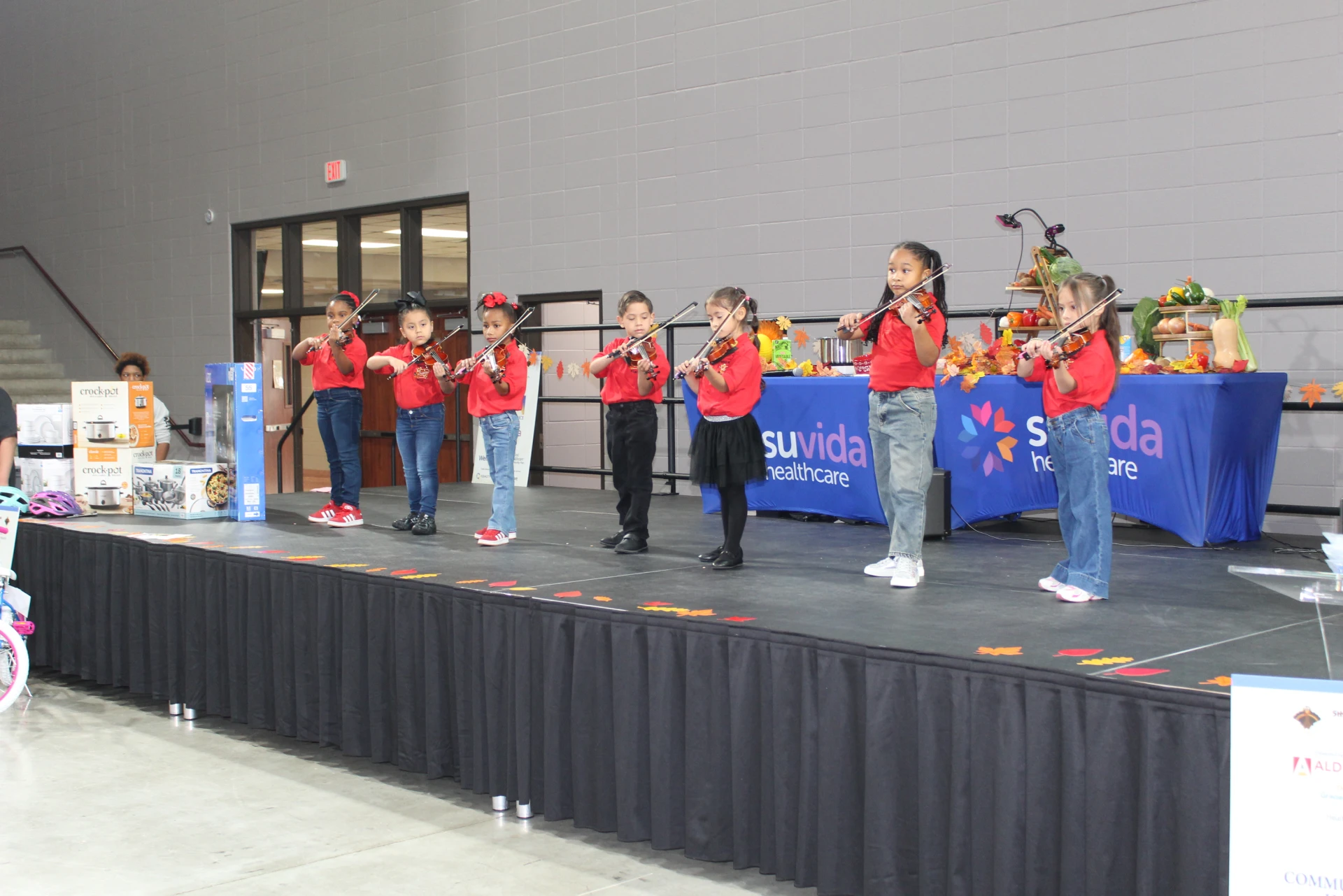 Group of children in red shirts performing on violins on stage during the Equality Health Foundation Houston Fall Festival 2026.